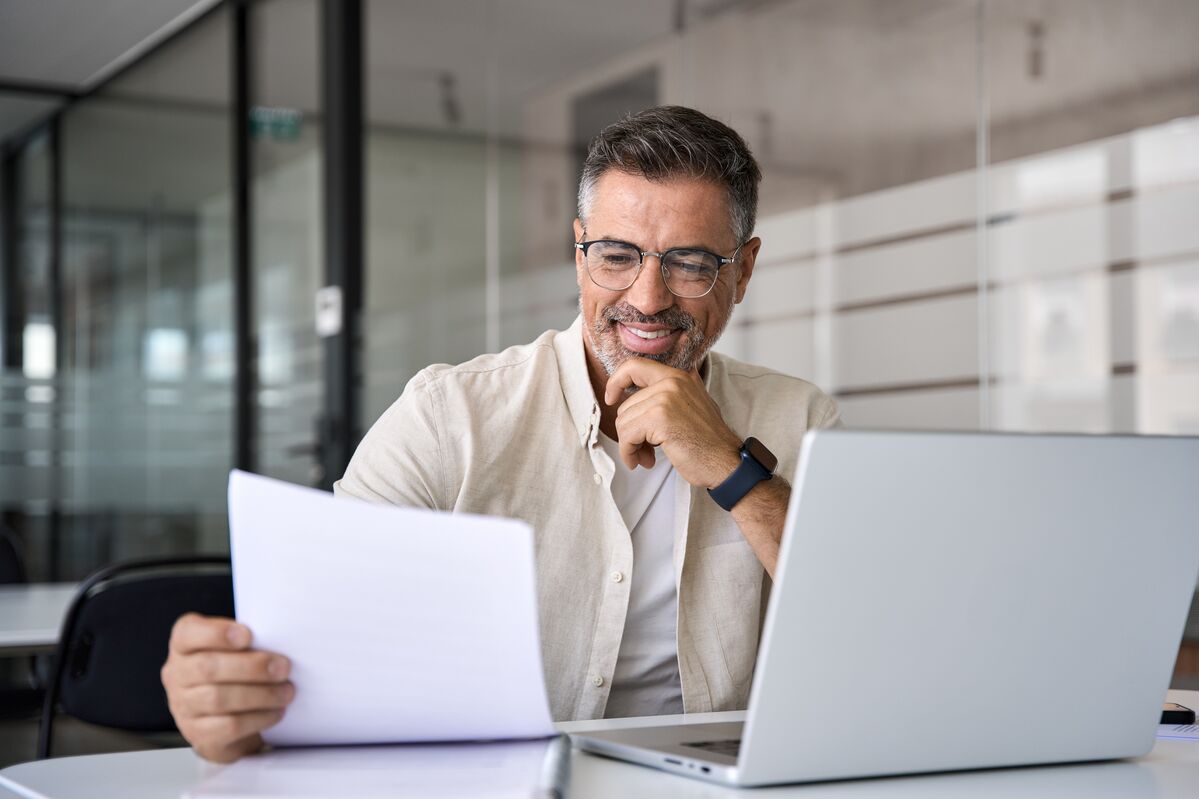 Smiling older man looking at paperwork and laptop